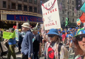 Members of El Sol Brillante walk down a crowded Manhattan street carrying signs and banners protesting the continued use of fossil fuels