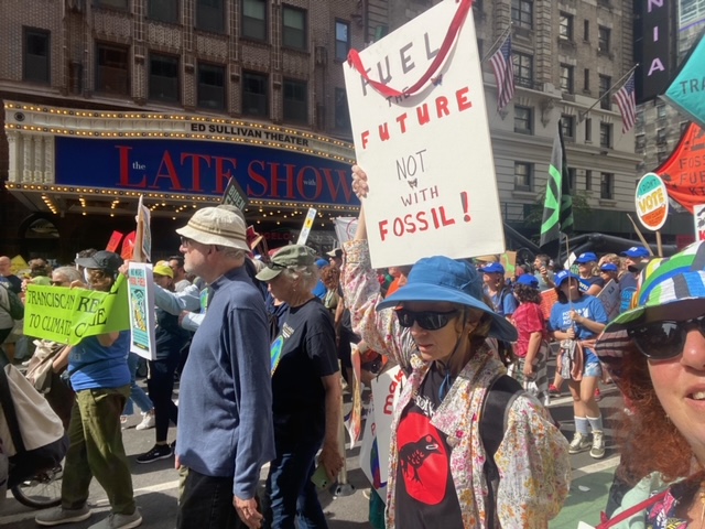 Members of El Sol Brillante walk down a crowded Manhattan street carrying signs and banners protesting the continued use of fossil fuels